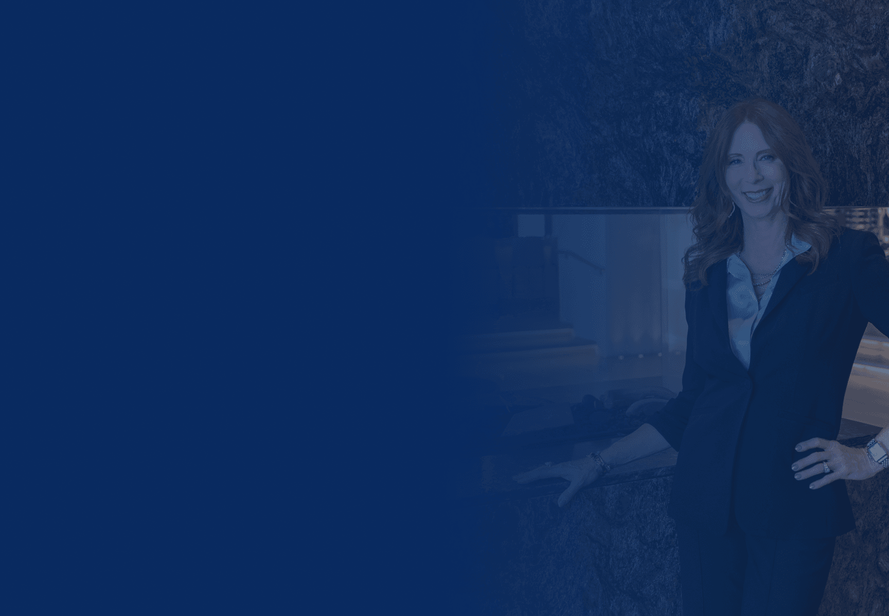 Smiling professional woman in a dark suit standing confidently against a dark, textured wall with a blue overlay.